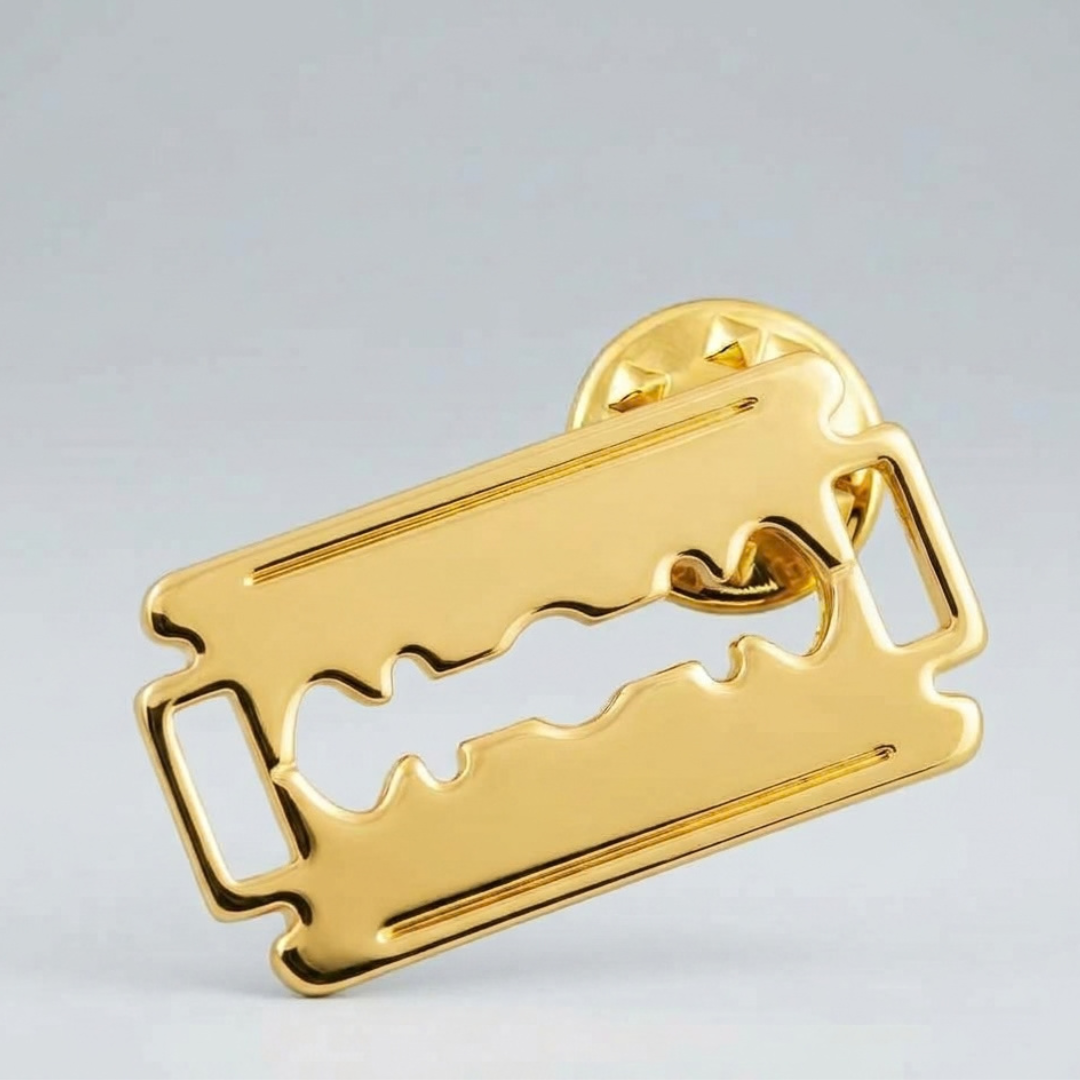 Gold double edge razor blade label pin shown on a grey background