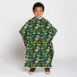 A young child wearing a dark green poncho-style blanket with a colorful cartoon dinosaur pattern, standing against a light gray studio background.