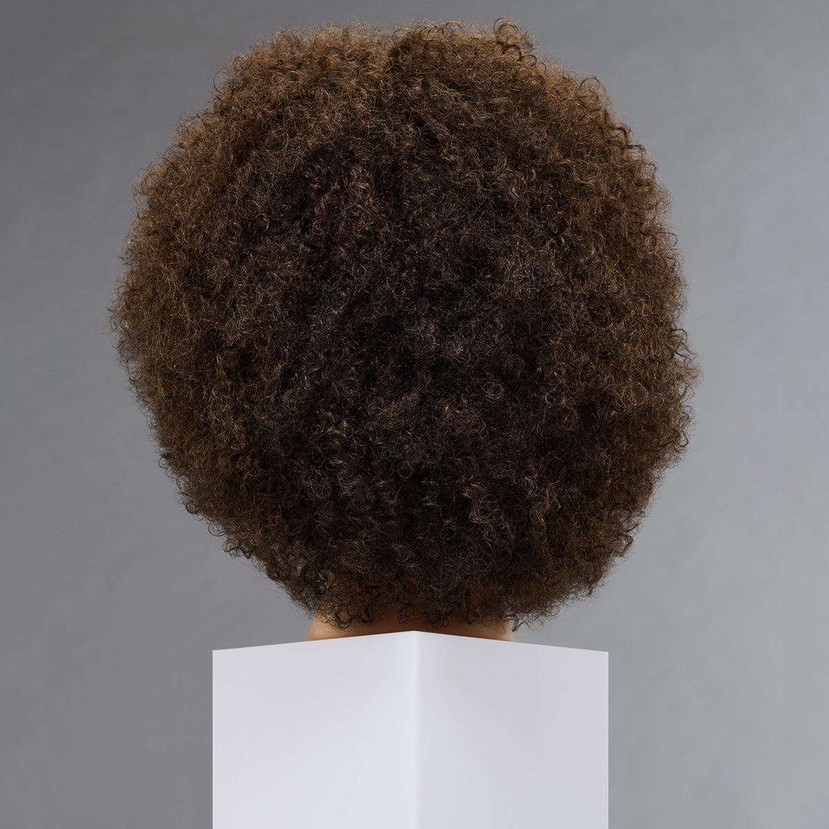 A dark brown textured afro wig displayed on a white mannequin head against a neutral gray background.