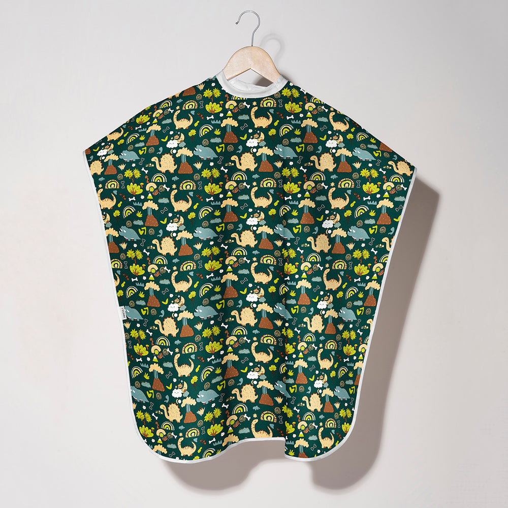 A baby bib or cape with a forest-themed pattern, hanging on a wooden hanger against a plain light gray wall.