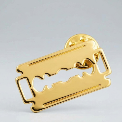 Gold double edge razor blade label pin shown on a grey background